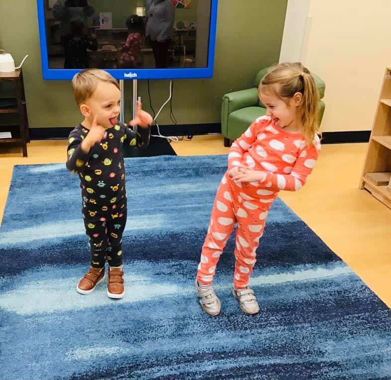 Two children in pajamas playing on a blue rug