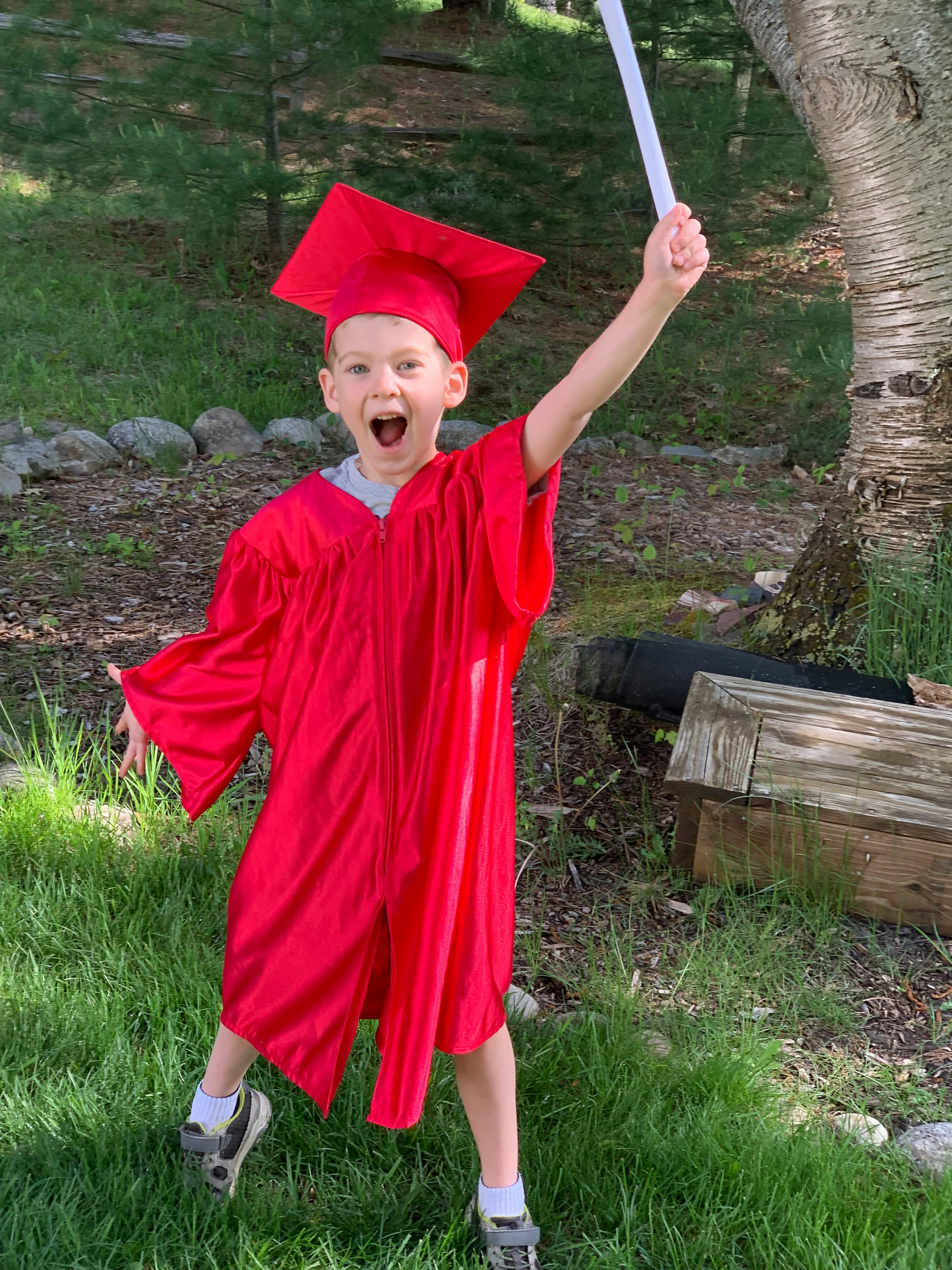 Child in a red graduation cap and gown holding up a diploma