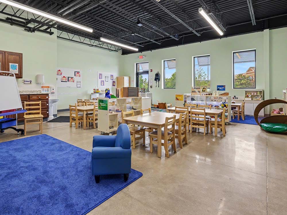 Empty classroom with small tables and chairs, and a blue rug