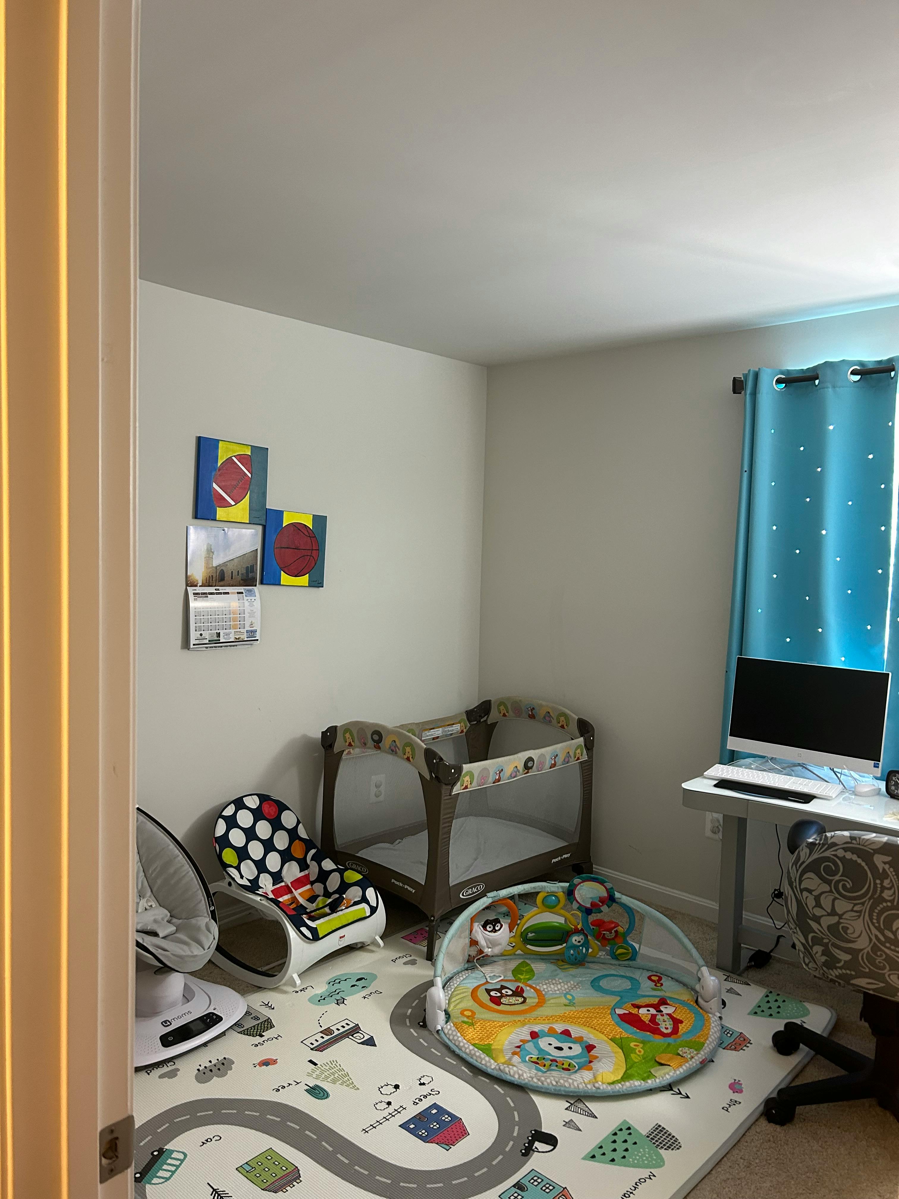 Nursery room with a crib, baby bouncer, play mat, and desk with computer