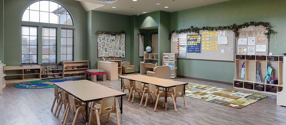 Classroom with small tables and chairs, large window, and bulletin boards
