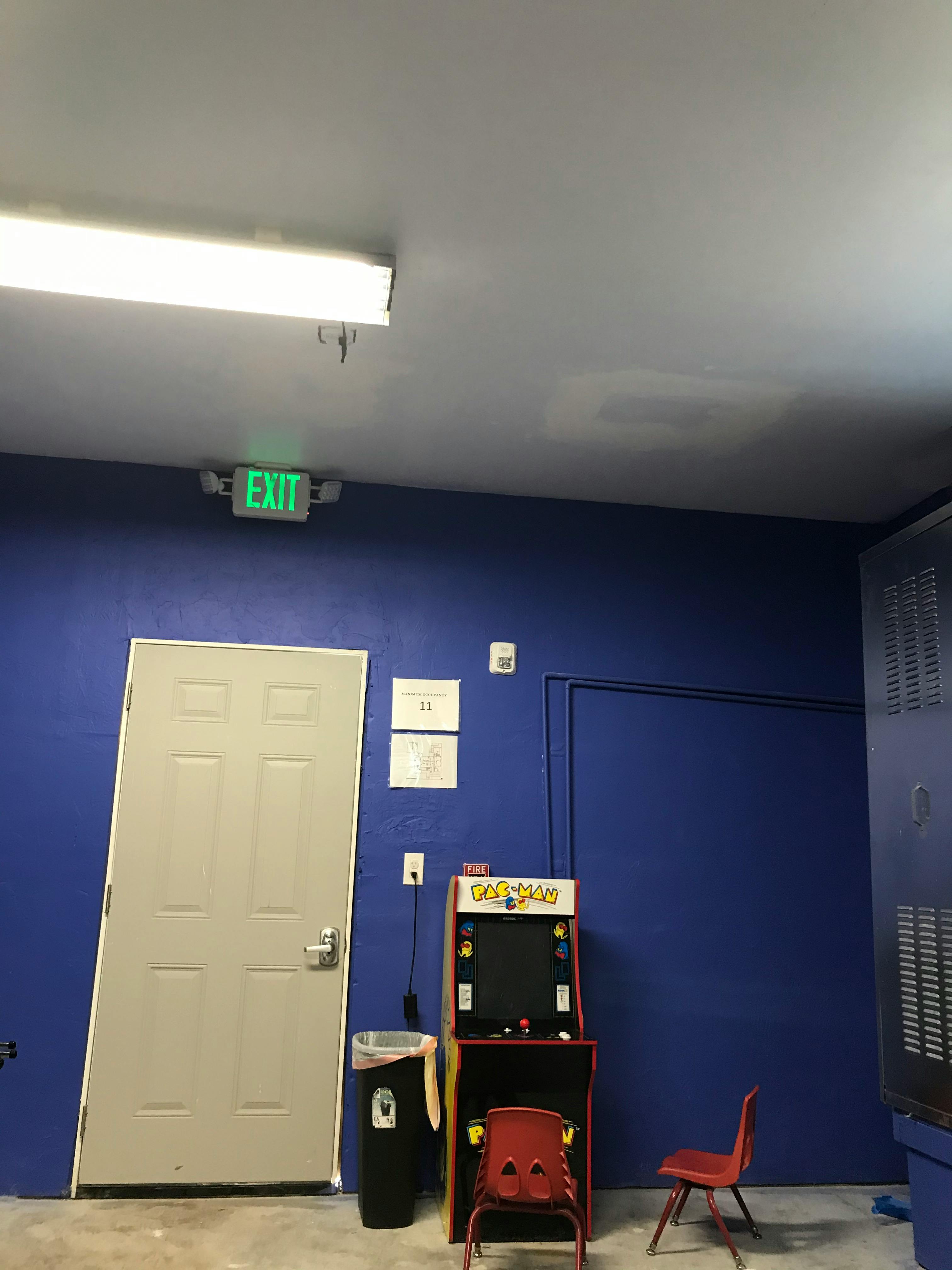 Exit sign above a door, arcade game, and chairs