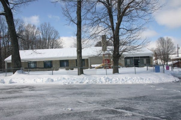 Building with snow on the roof and ground, bare trees in front