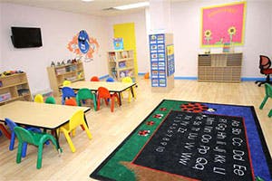 Empty classroom with small tables and chairs, alphabet rug