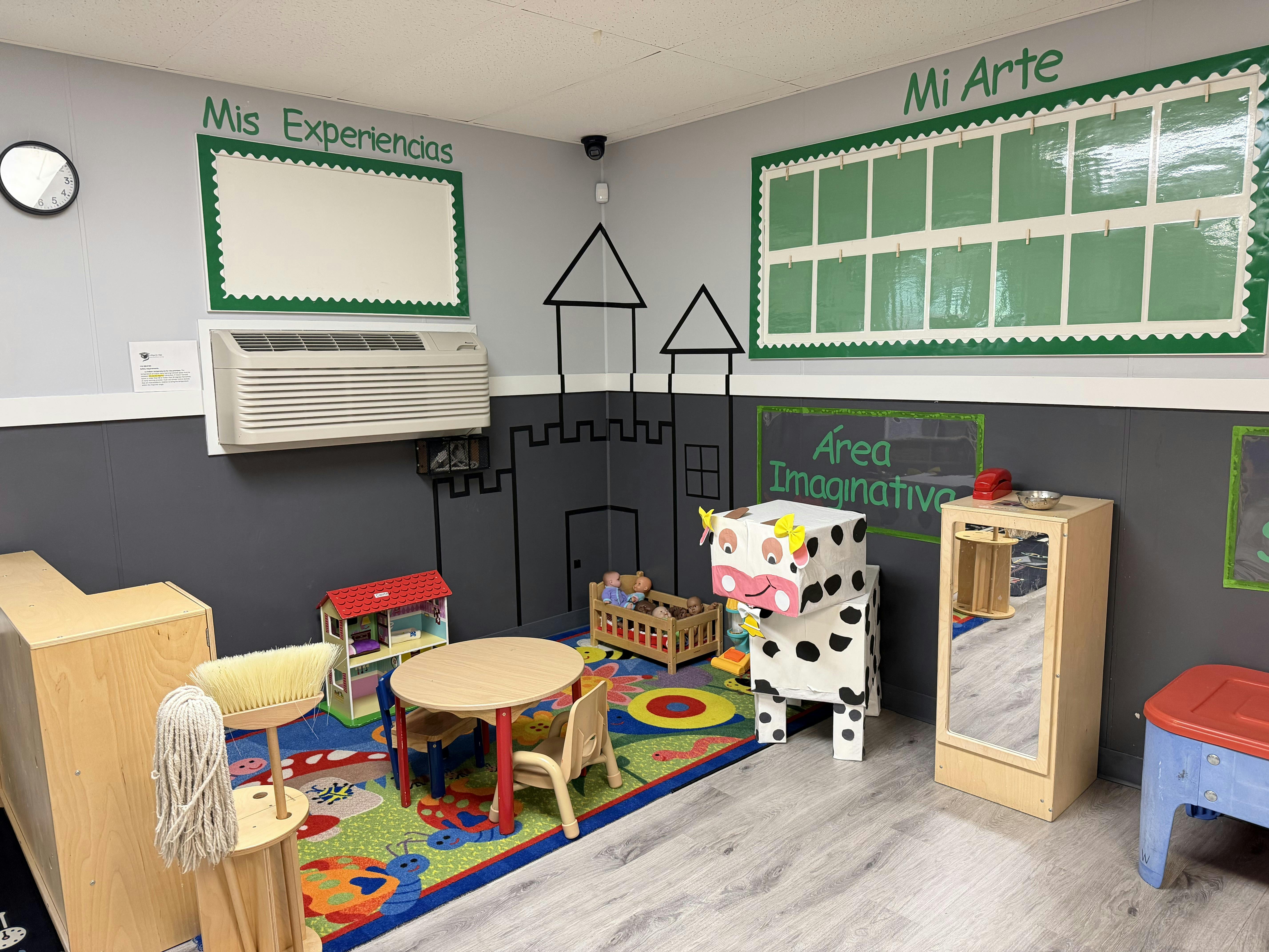 Classroom play area with a small table, dollhouse, and cow-themed box toy