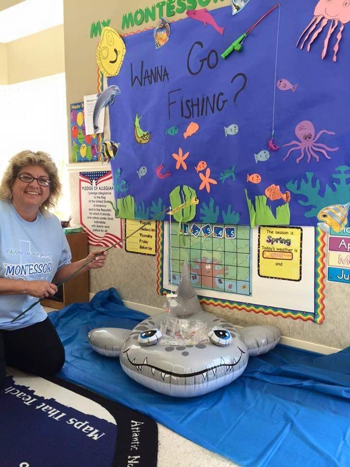 Person holding a fishing rod next to an inflatable shark and a "Wanna Go Fishing?" sign