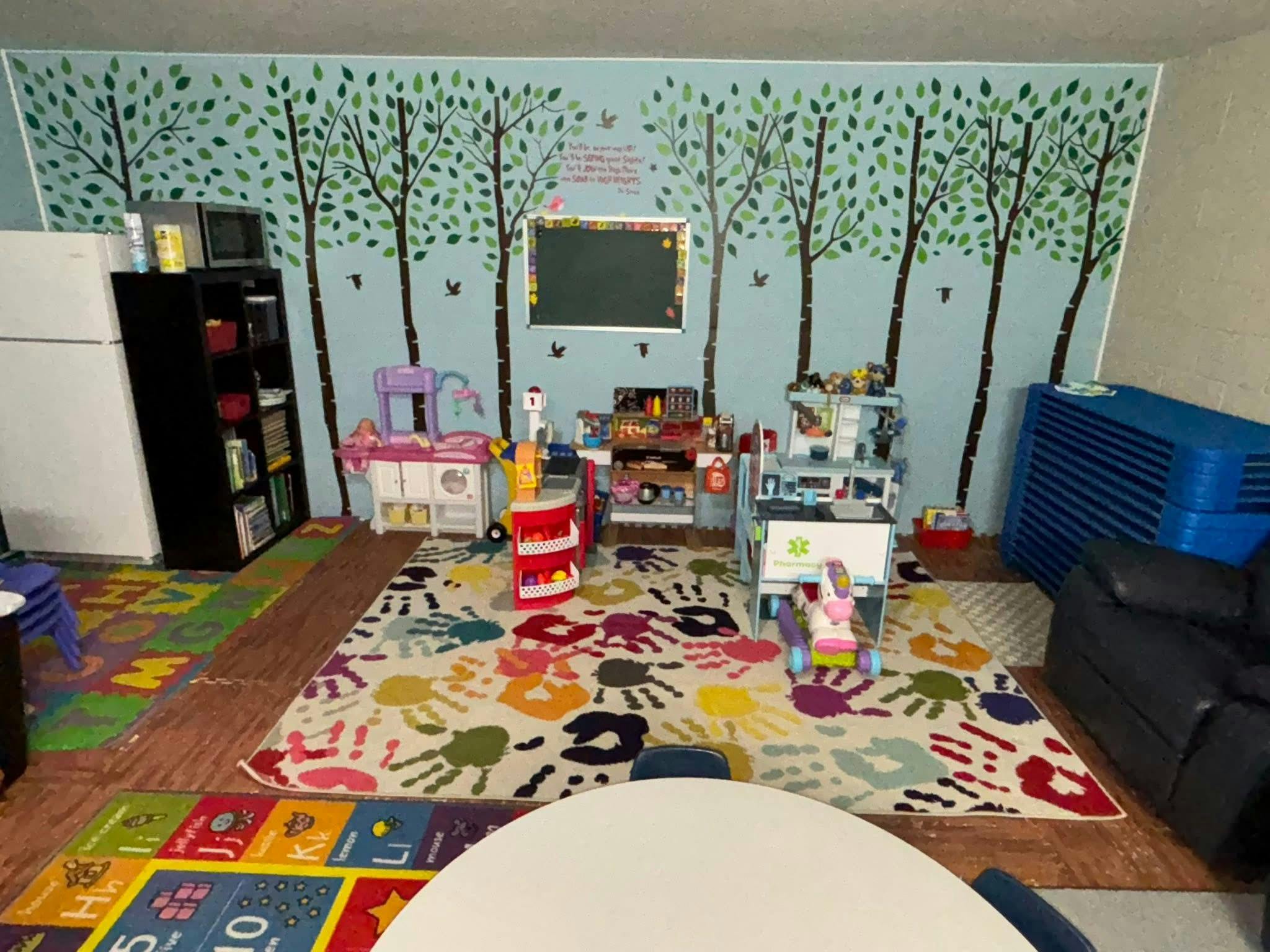 Children's play area with a tree mural on the wall, colorful rug, and toys