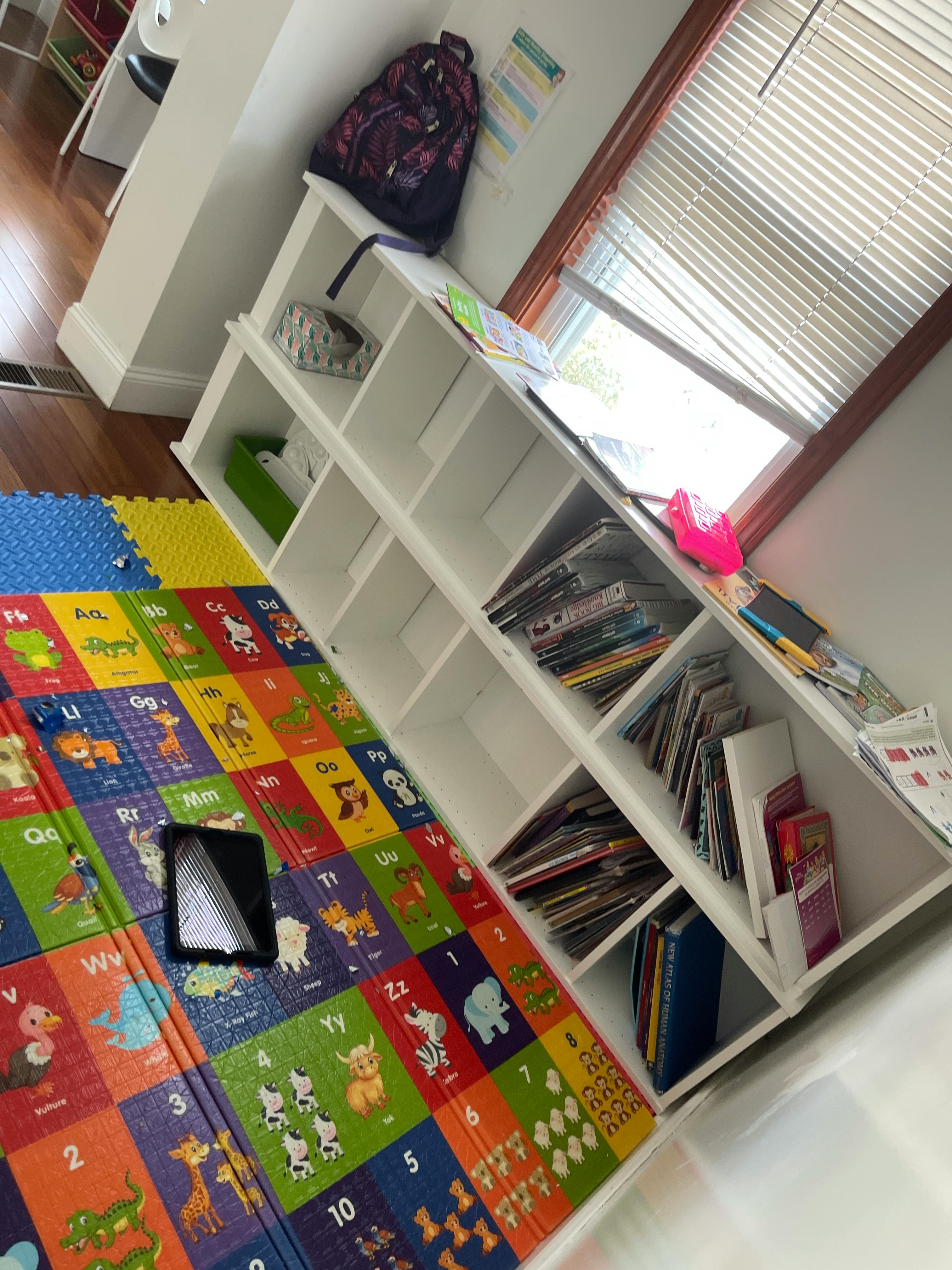 Colorful alphabet playmat next to a white bookshelf with books and magazines