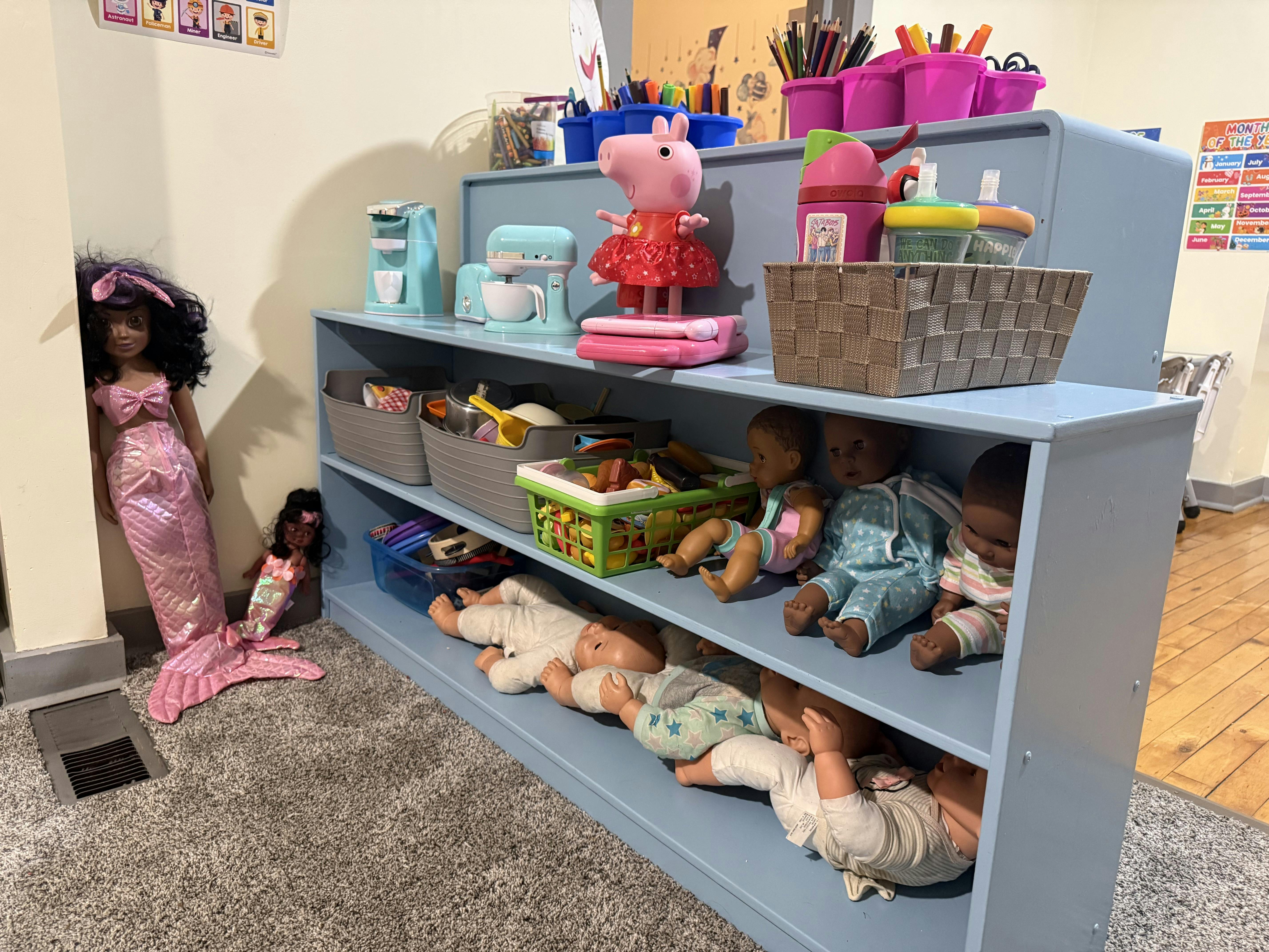 Mermaid dolls and baby dolls on and around a blue toy shelf
