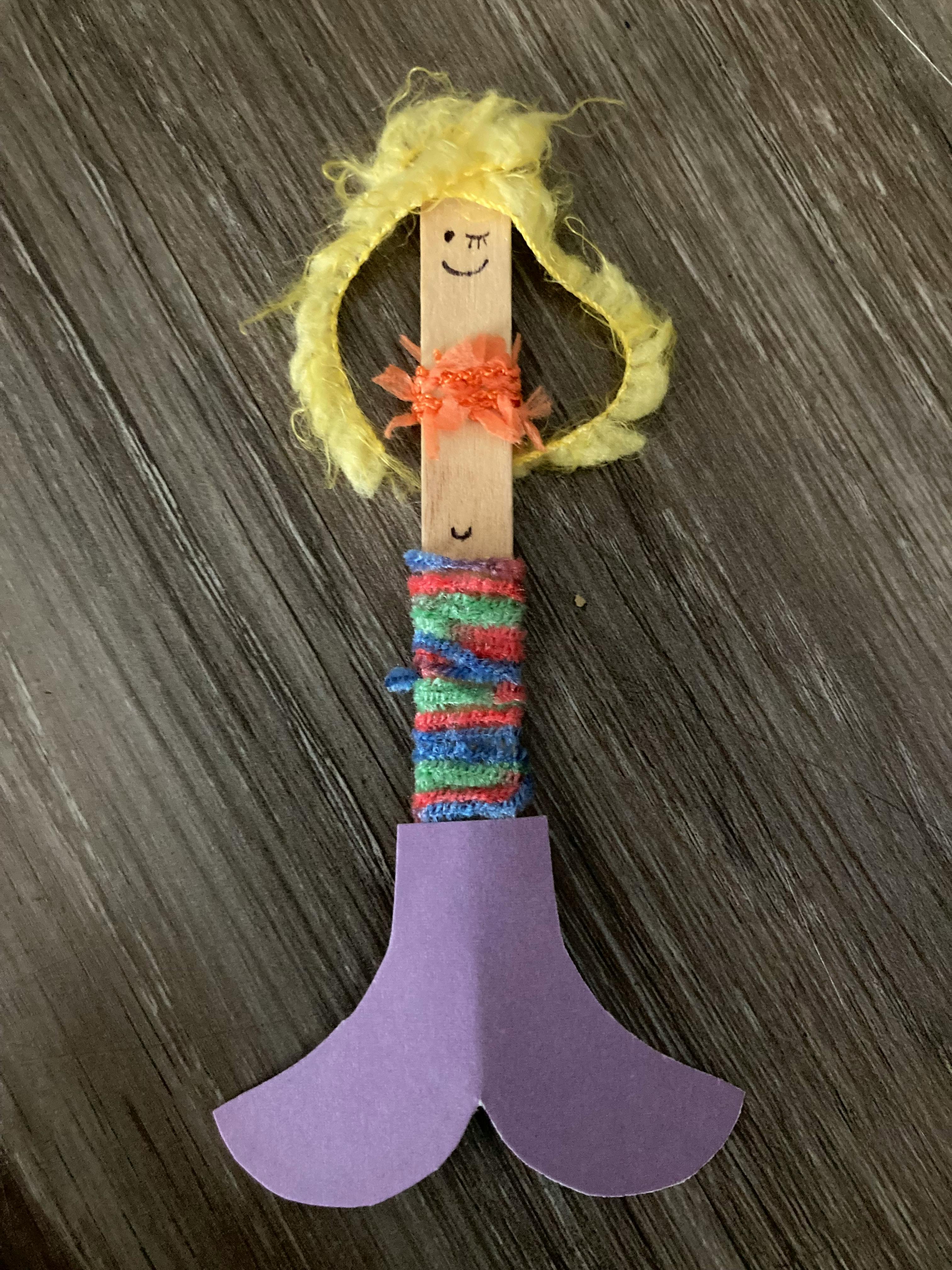 Craft stick with a drawn face, yarn hair, and a purple paper mermaid tail