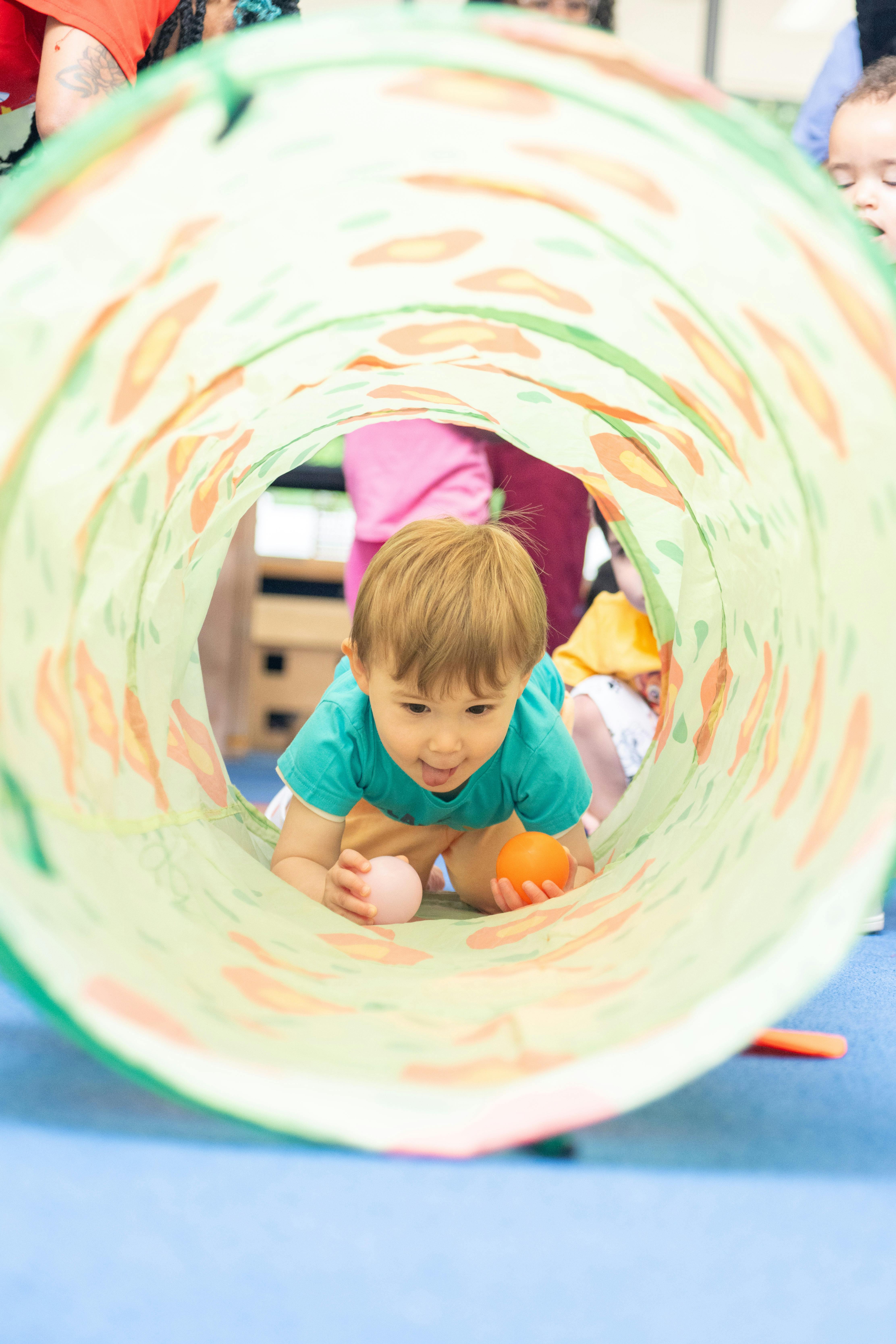Child crawling through a play tunnel with two balls