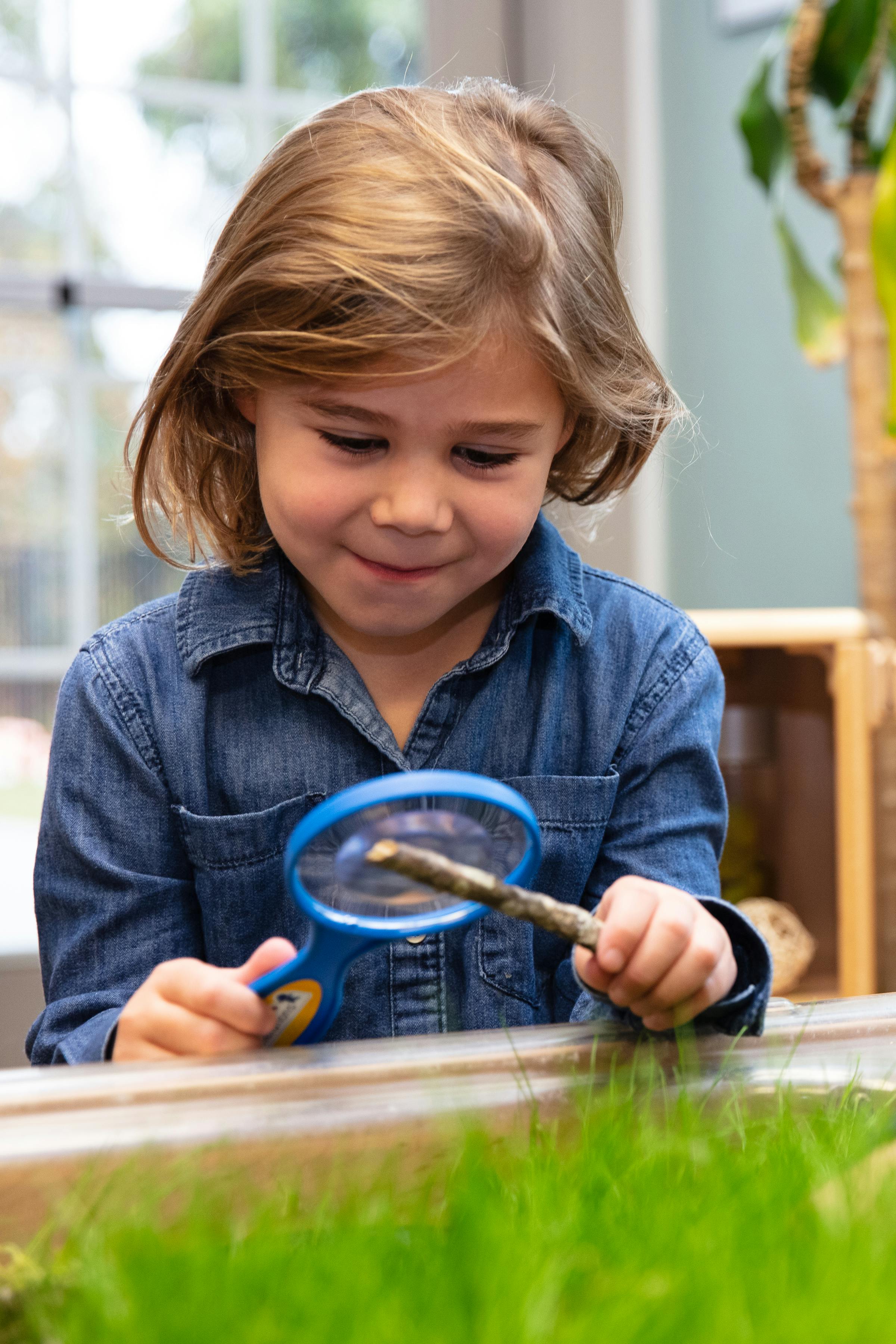 Child in denim shirt holding a magnifying glass to a stick