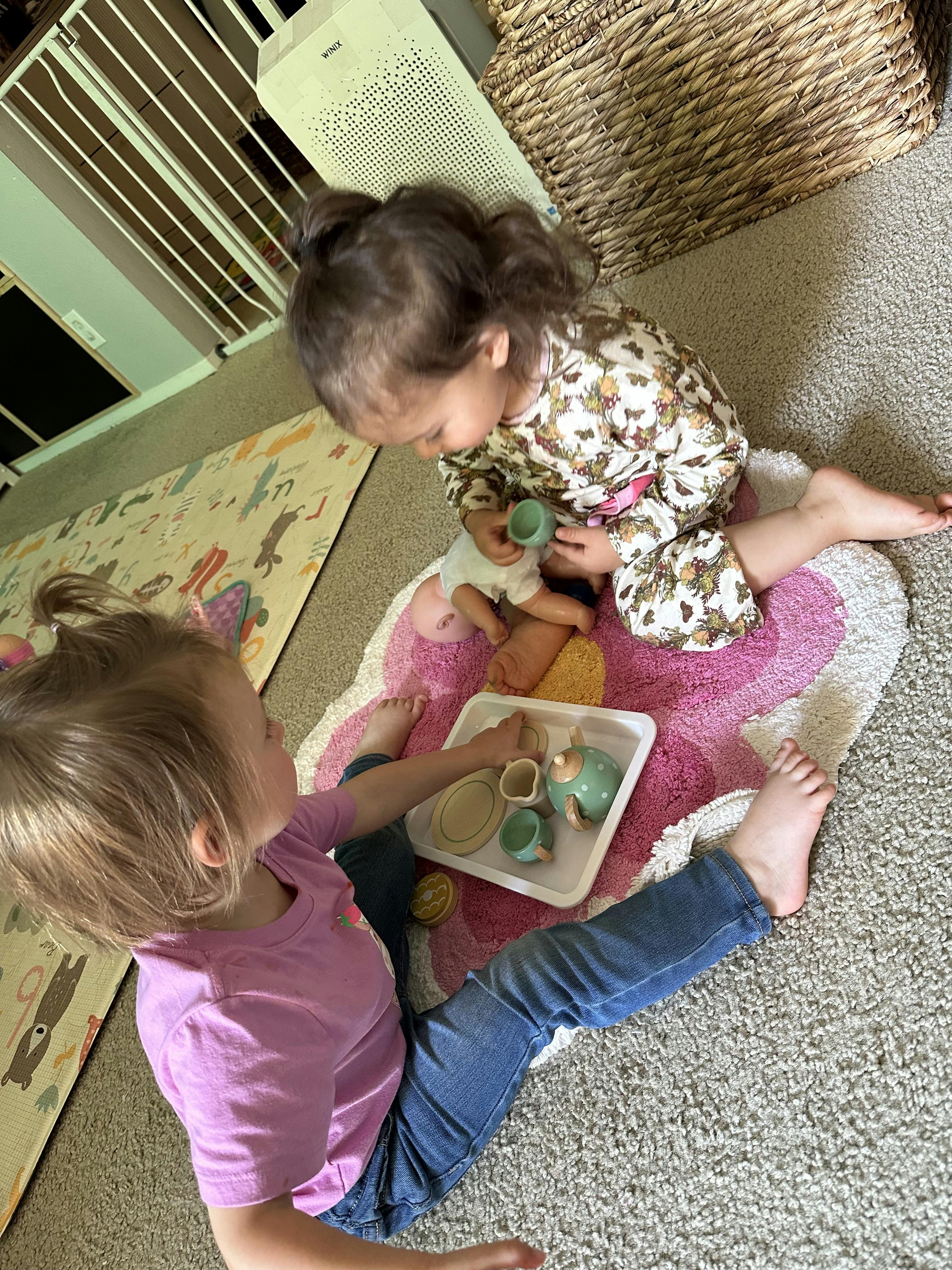 Two children playing with a toy tea set on a rug