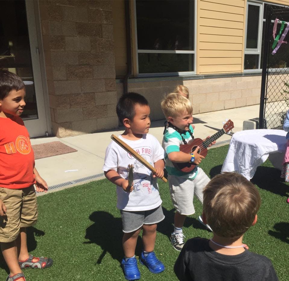 Children playing outside, one holding a stick, another playing a ukulele