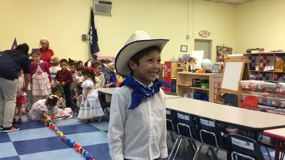 Child in a cowboy hat and blue bandana in a classroom with other children