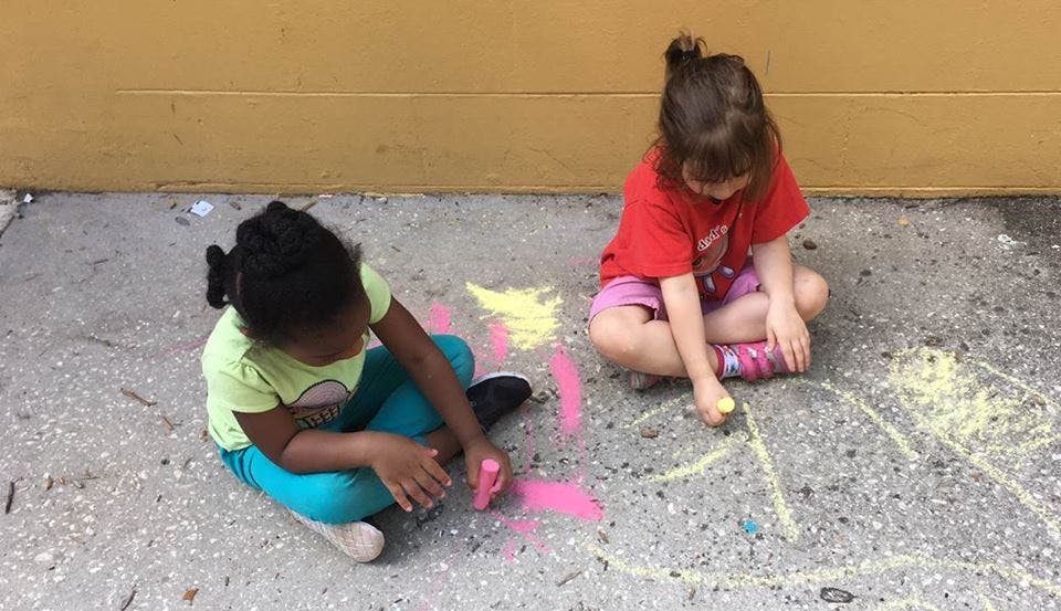 Two children drawing with chalk on pavement