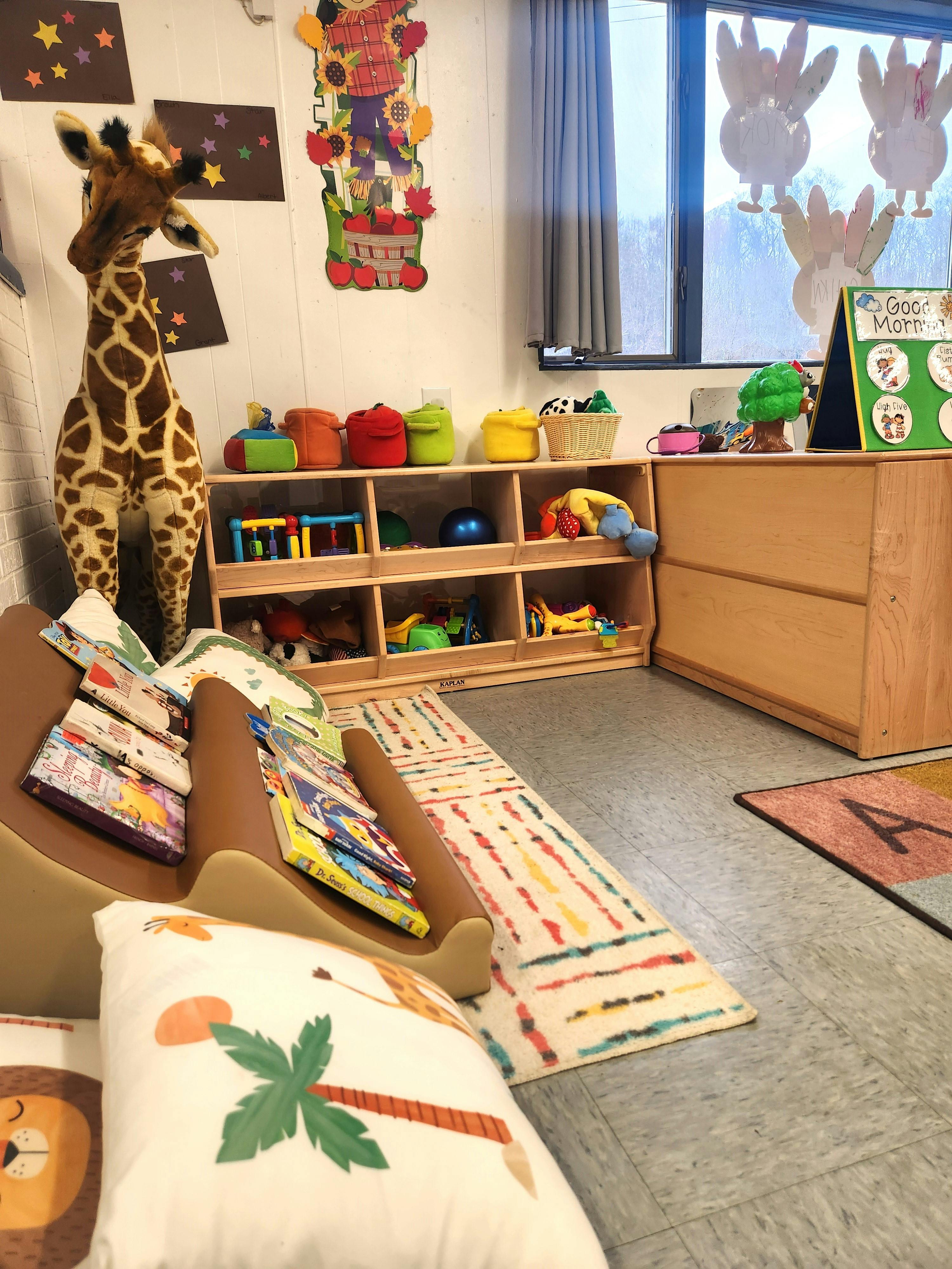 Classroom with a giraffe toy, bookshelves, and rugs