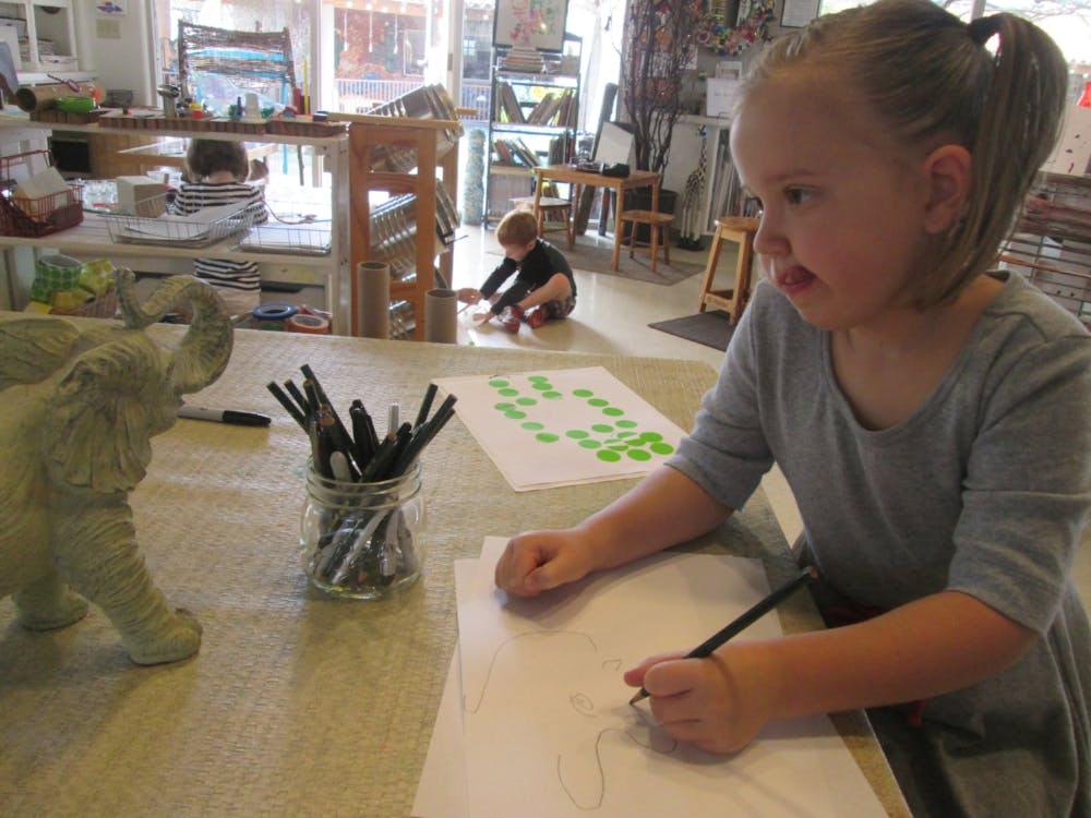 Child drawing at a table with another child in the background
