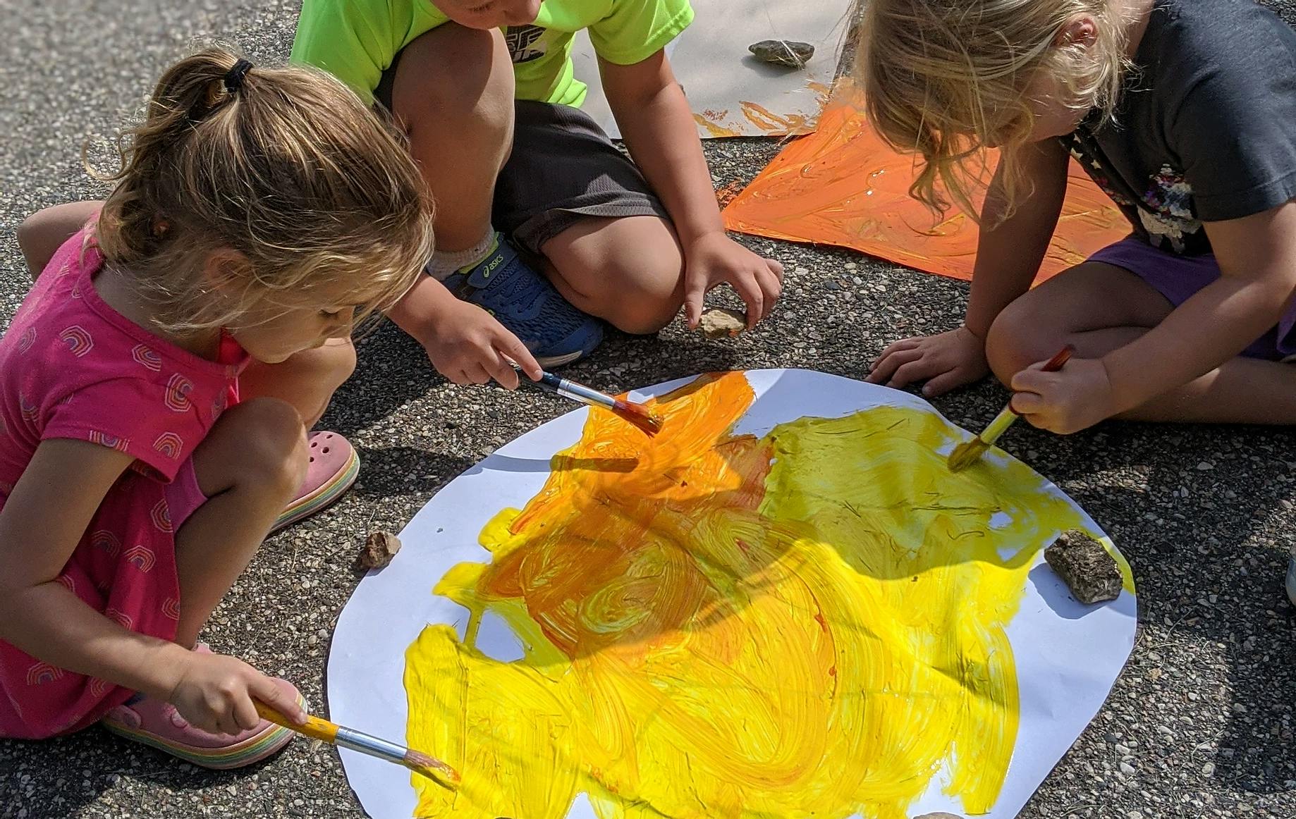 Children painting on a large piece of paper outdoors
