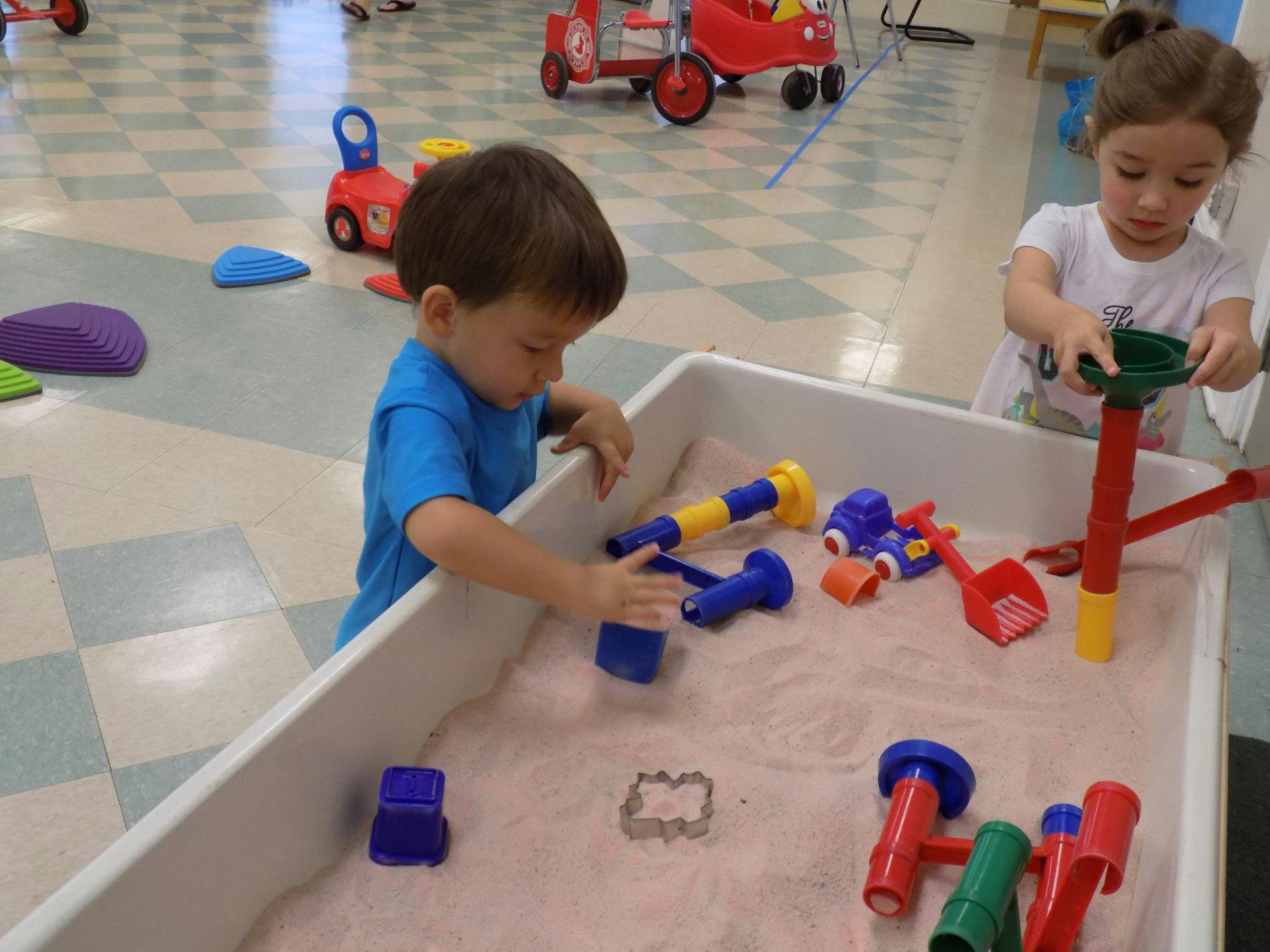Two children playing in a sand table with toys