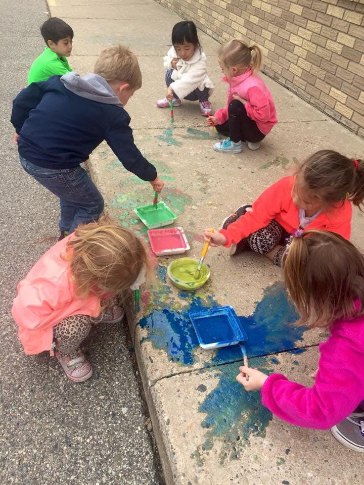 Children painting on a sidewalk with brushes and paint trays