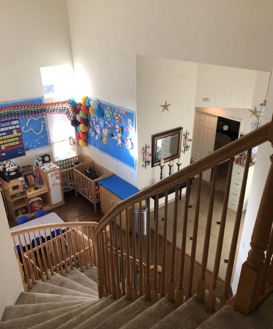 View from top of carpeted stairs looking down into a room with cribs