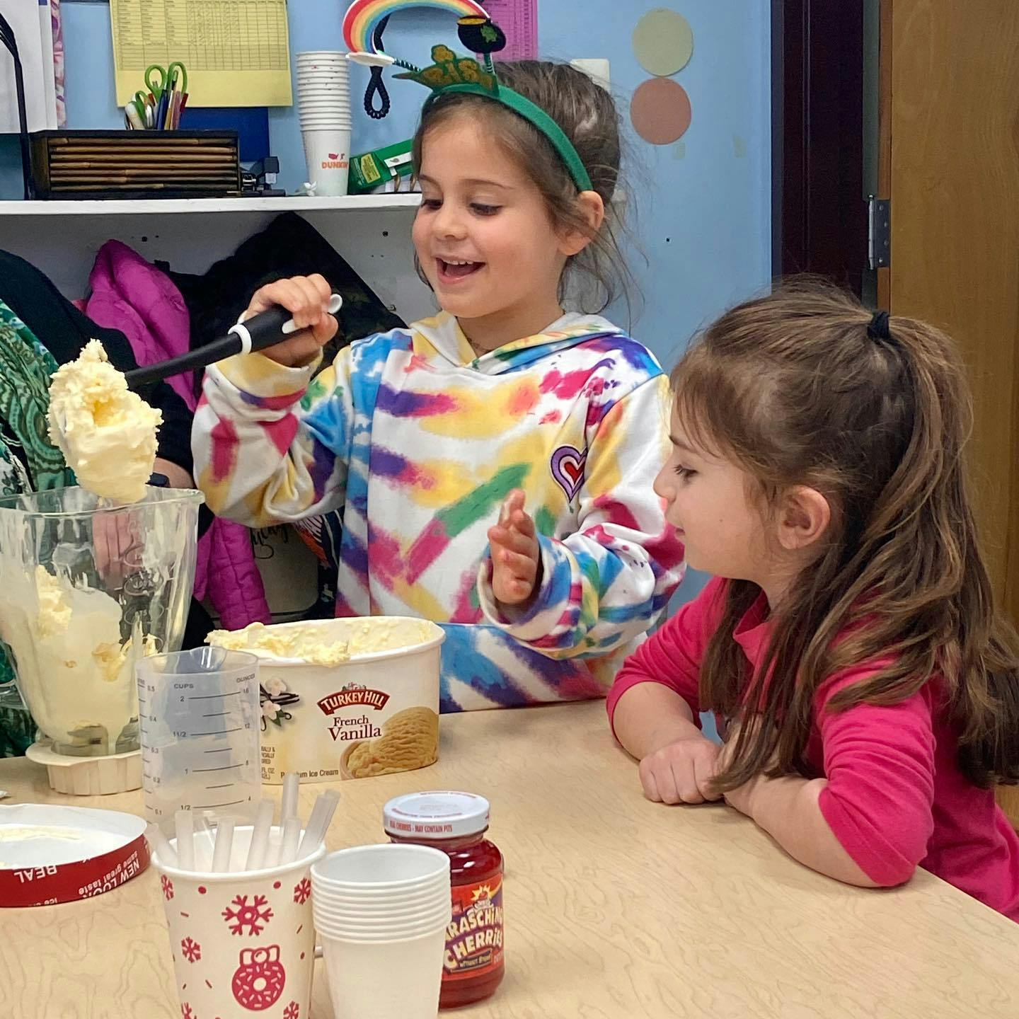 Child scooping ice cream into a cup, another child watching