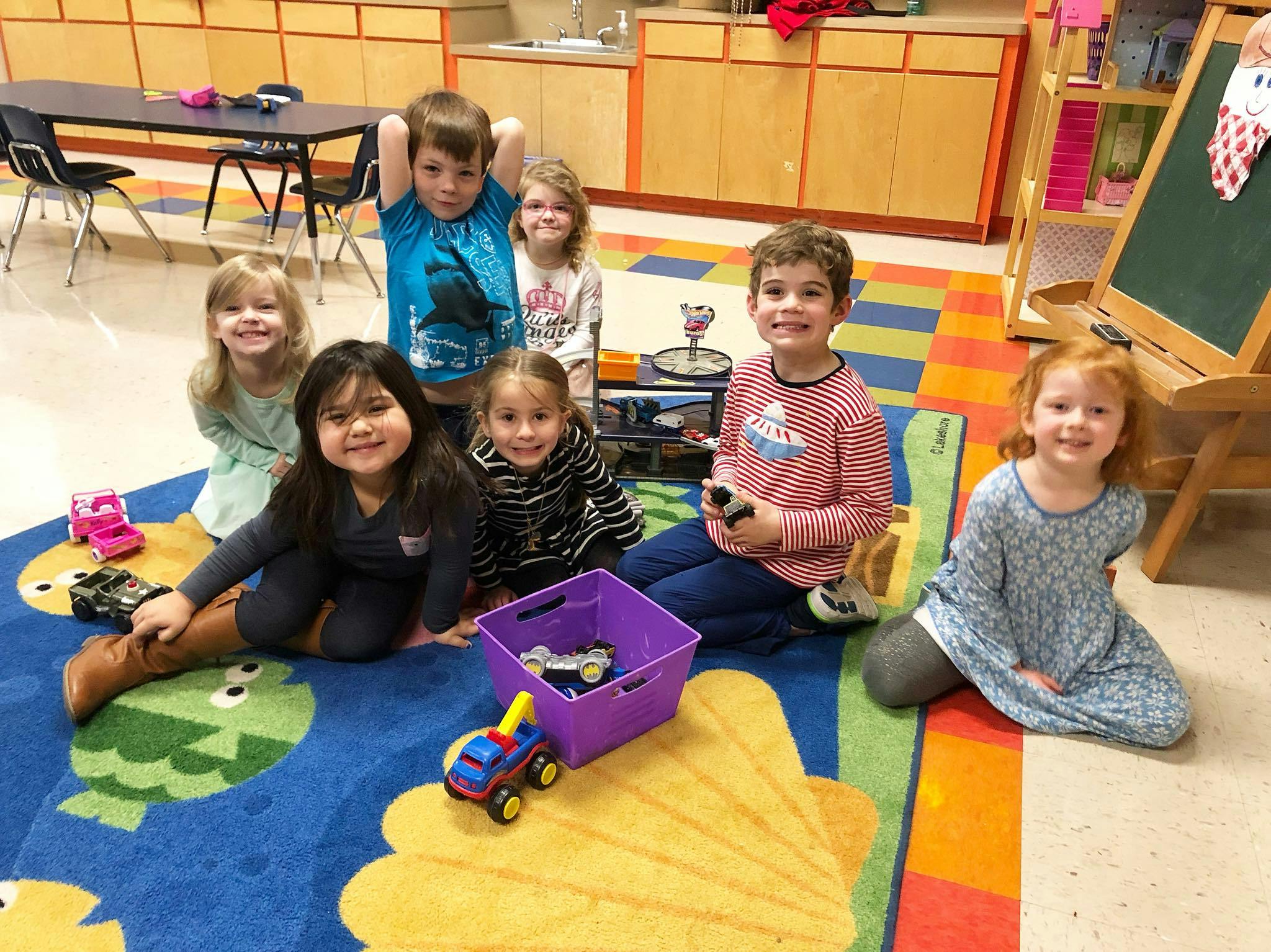 Six children sitting on a colorful rug in a classroom