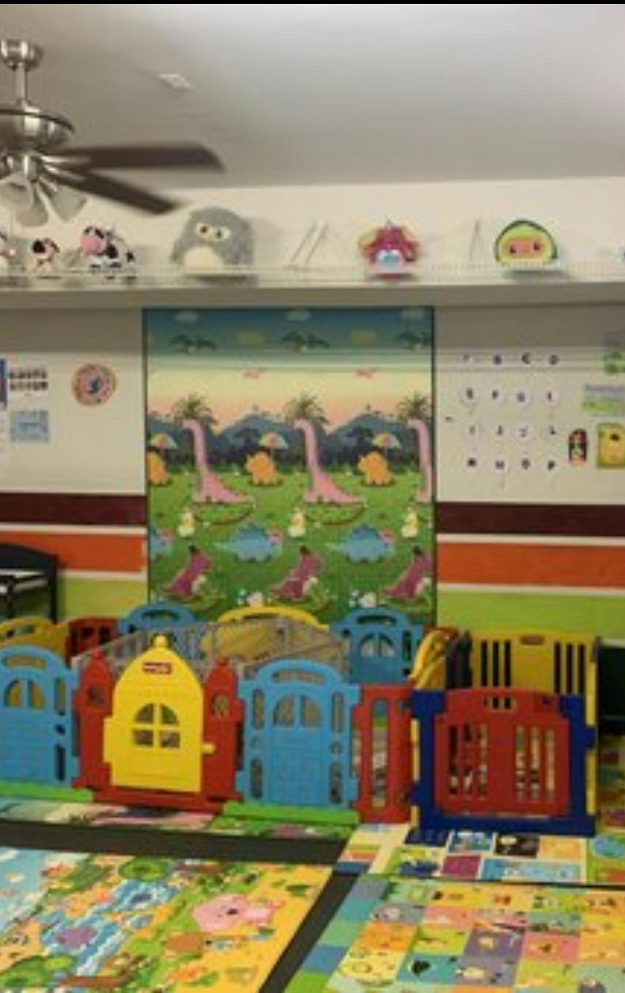 Colorful plastic playpen in a room with dinosaur wall art and plush toys