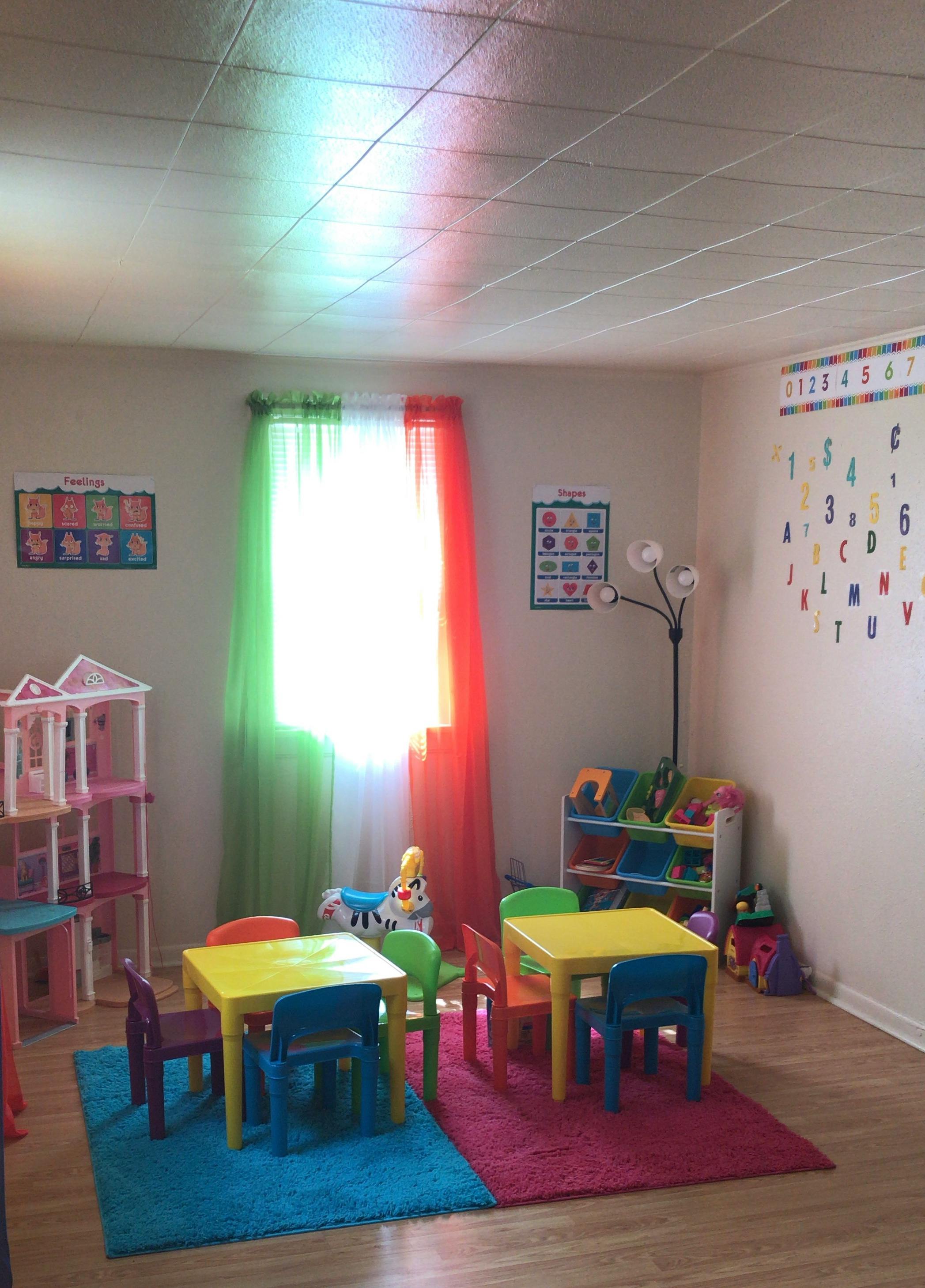Children's play area with small tables and chairs, toys, and colorful curtains