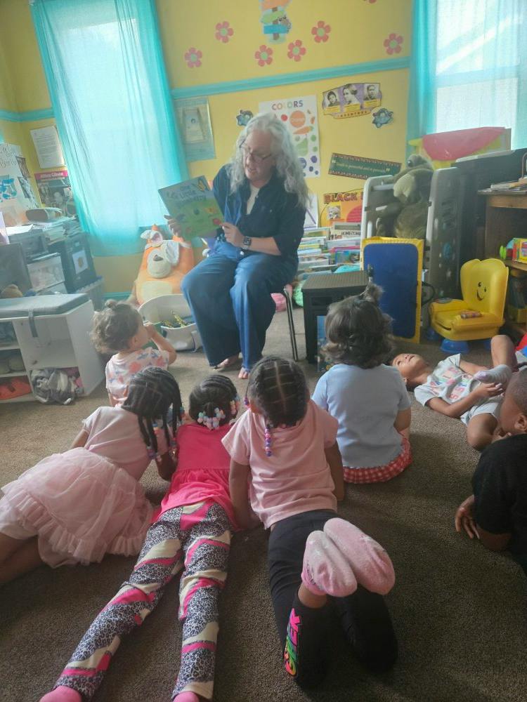Adult reading a book to a group of children sitting on the floor in a classroom