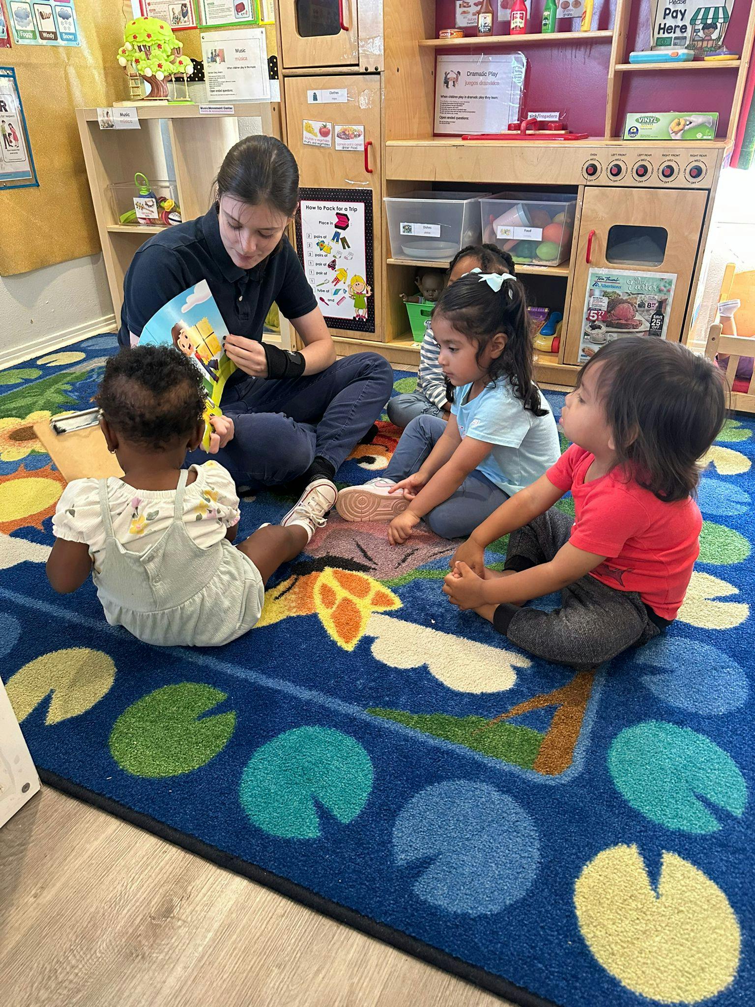 Person reading a book to three children in a classroom