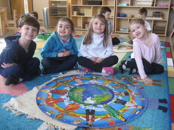Four children sitting on a rug around a circular world map puzzle
