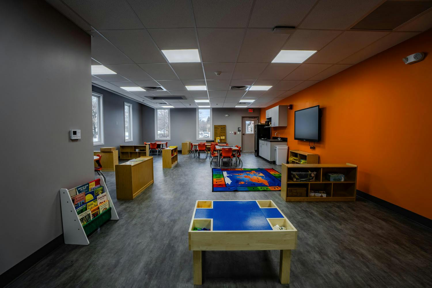 Classroom with small tables and chairs, a play rug, and a LEGO table