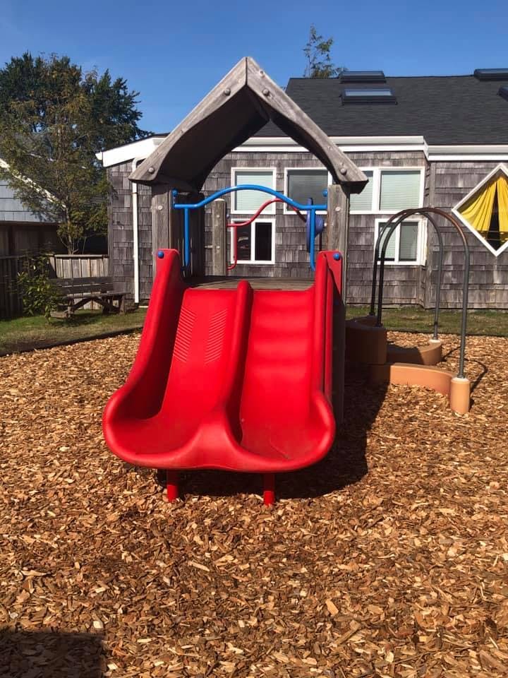 Red double slide on a playground with wood chips