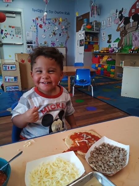 Child preparing a pizza at a table in a classroom