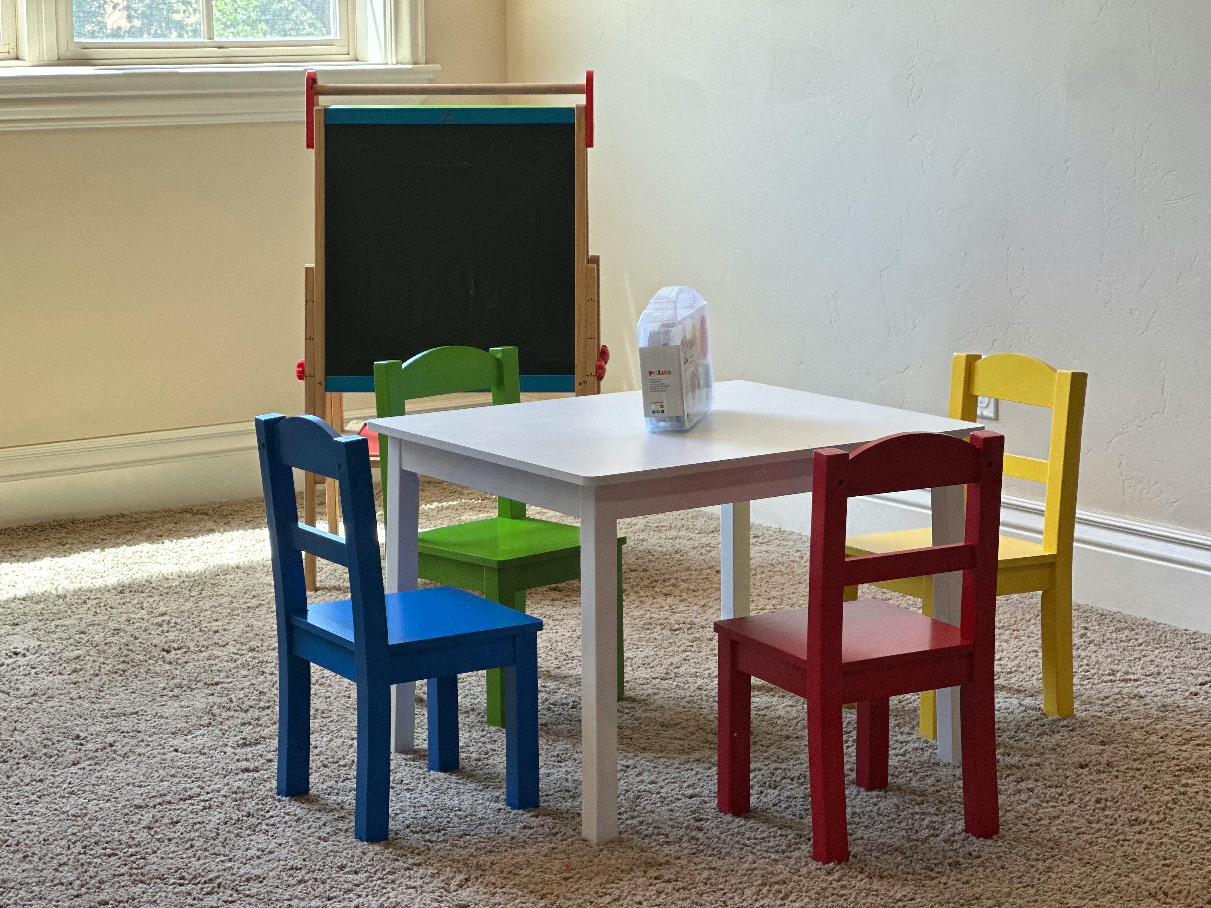 Small white table with four colorful chairs and an easel in a room