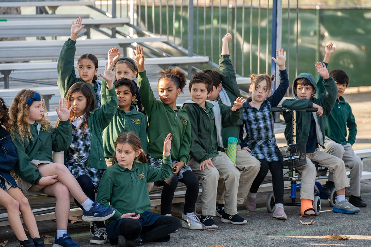 Group of children sitting on bleachers with hands raised