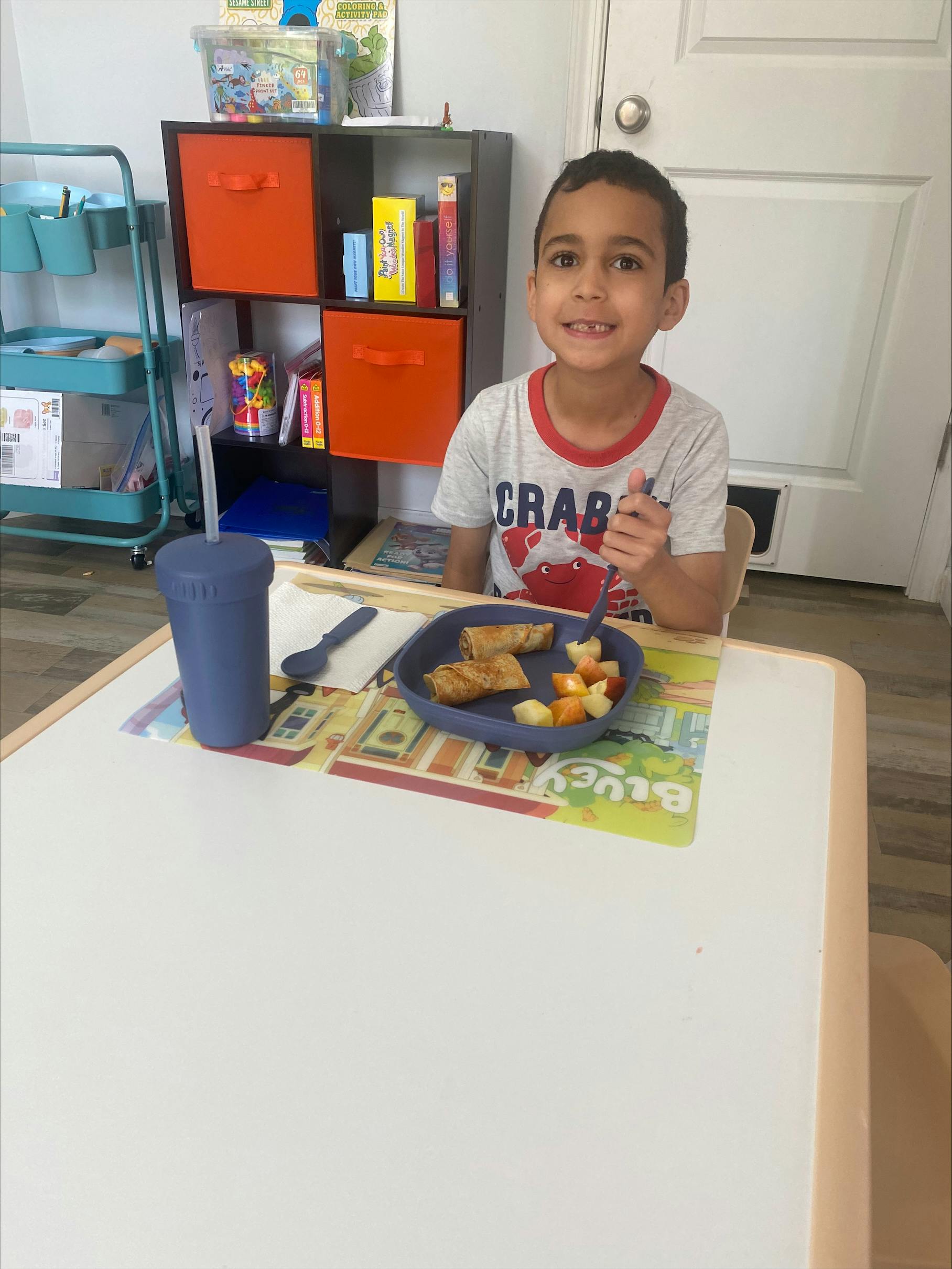 Child sitting at a table with a plate of food and a cup