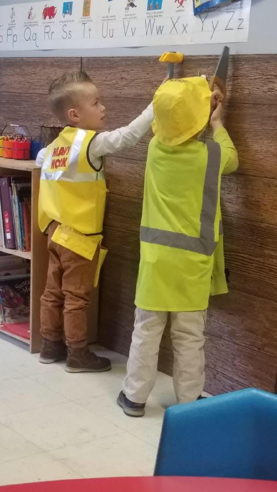 Two children playing with toy tools, one holding a saw and the other a hammer