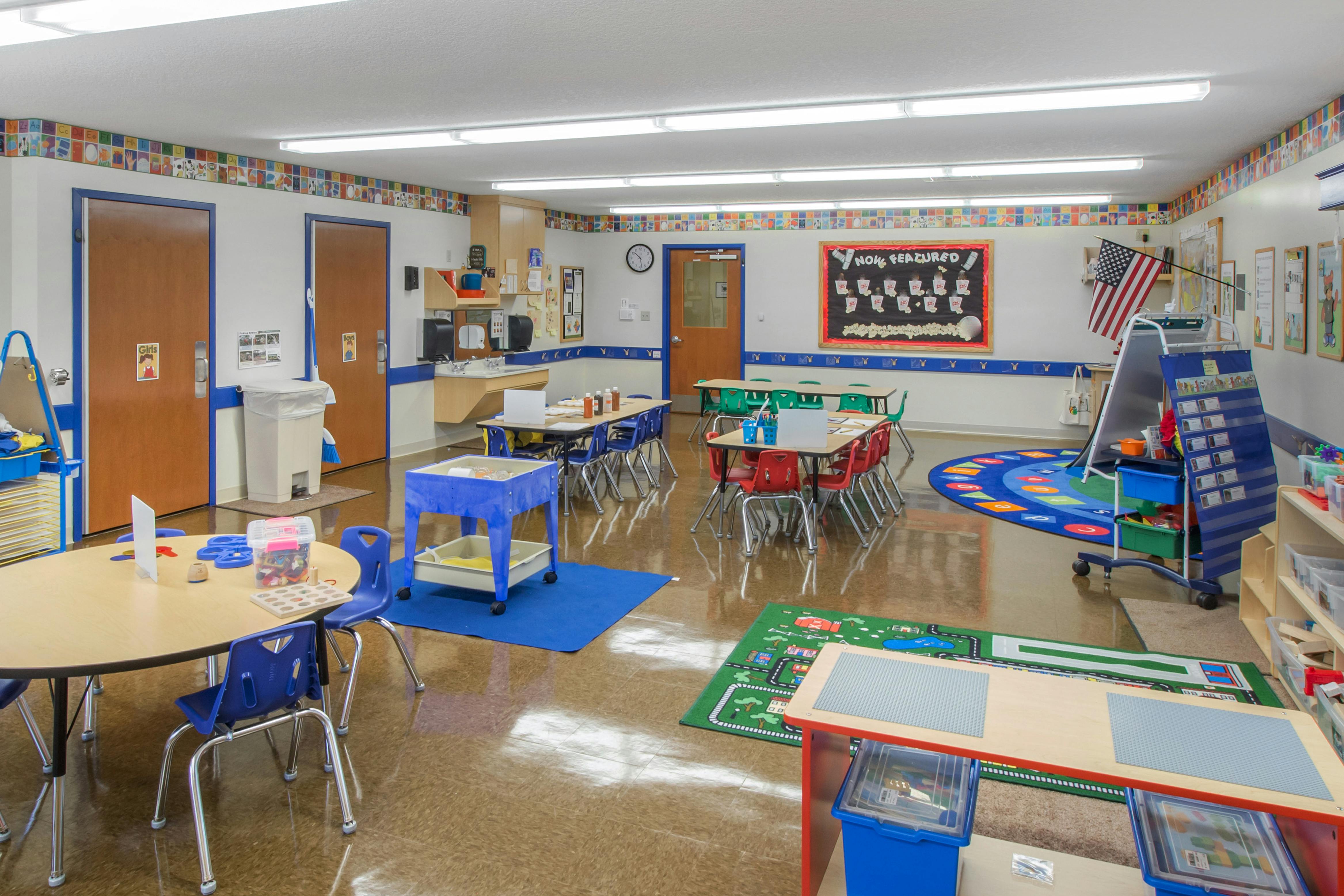 Classroom with small tables and chairs, a sink area, and various learning stations
