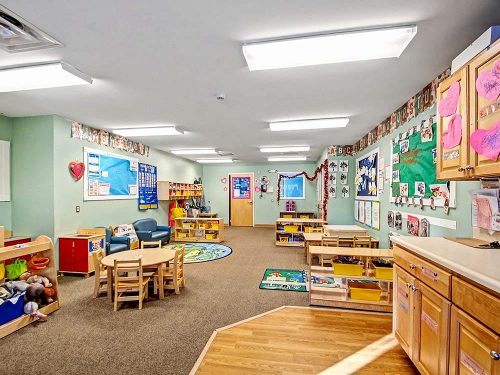 Classroom with small tables, chairs, and shelves with toys and learning materials