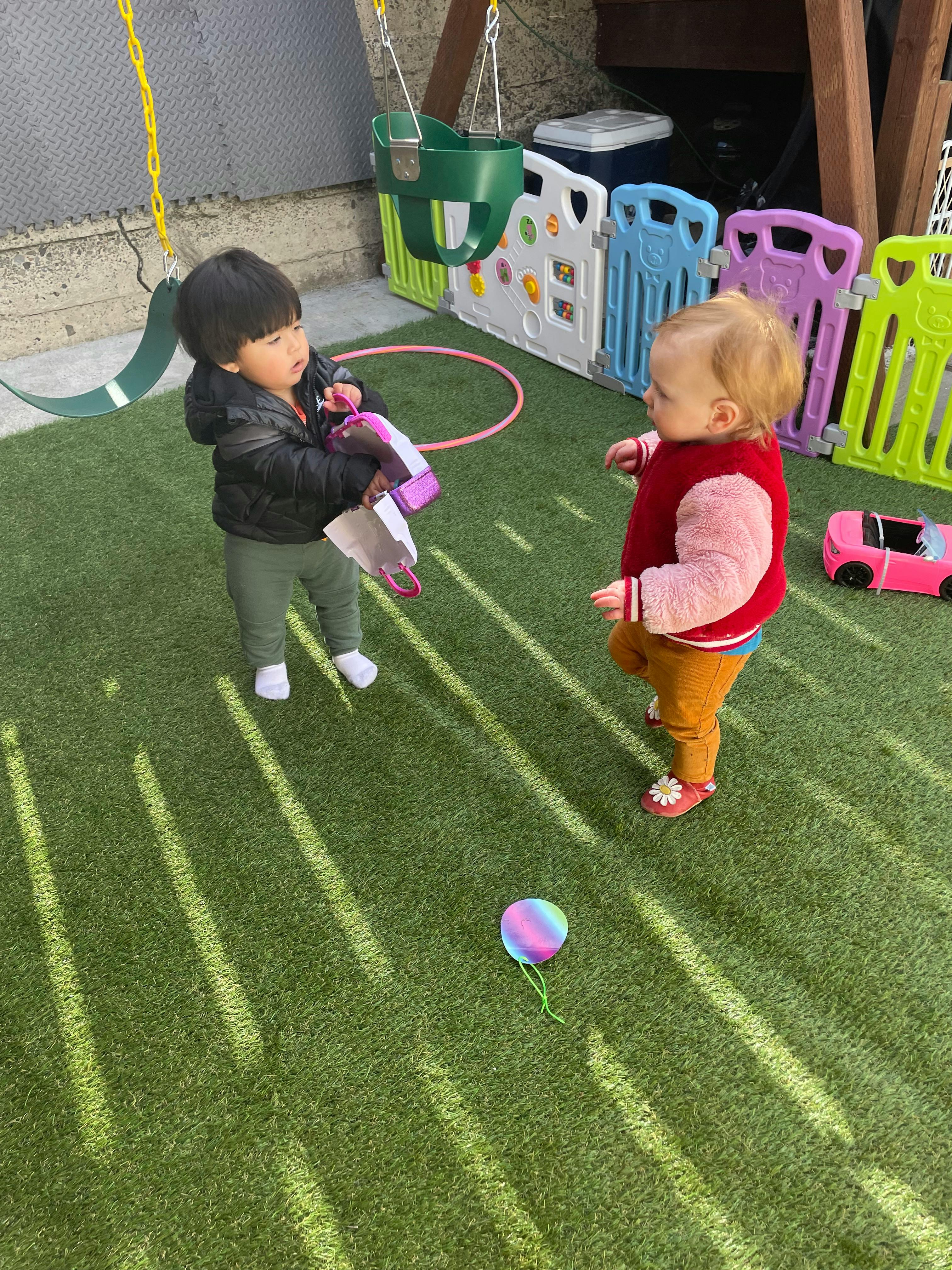 Two children standing on artificial grass, one holding a toy