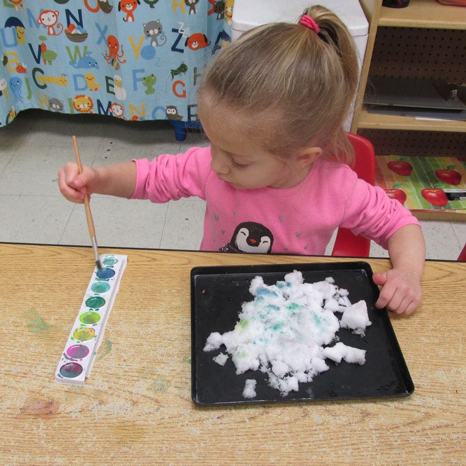 Child painting snow on a tray with watercolors