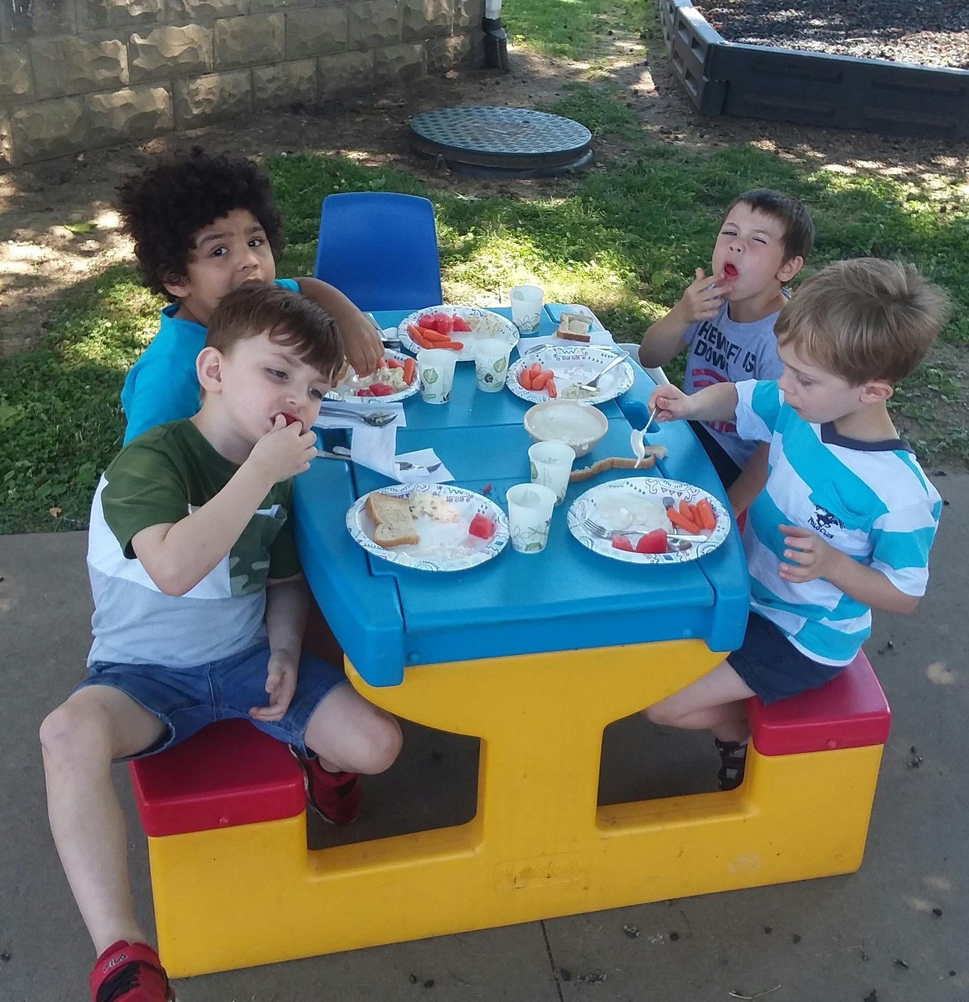 Four children eating at a picnic table outdoors