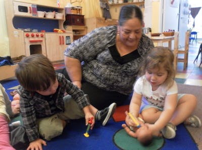 Adult and two children playing with toys on the floor in a classroom