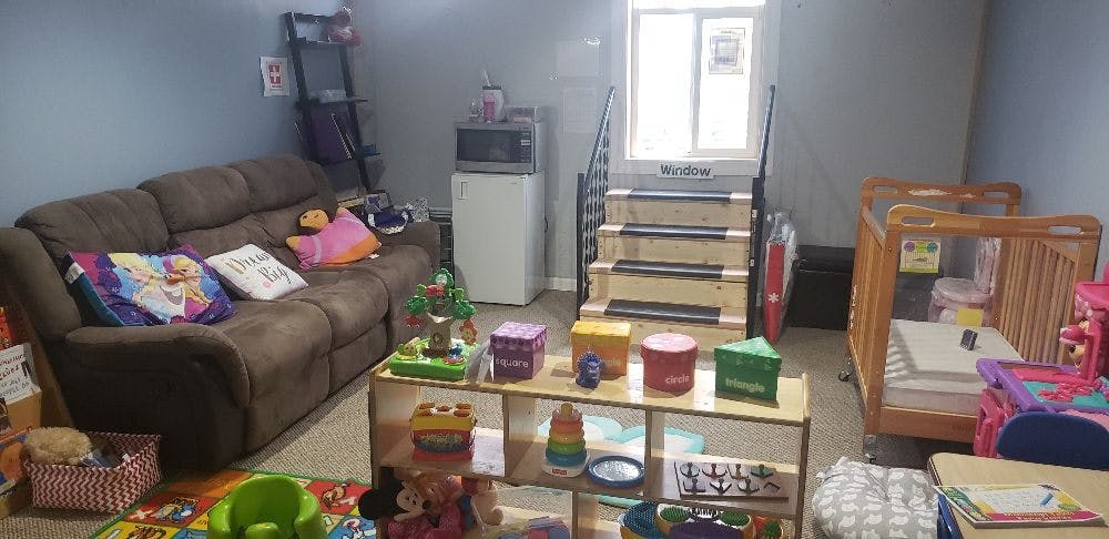 Living area with a brown sofa, small crib, and play items