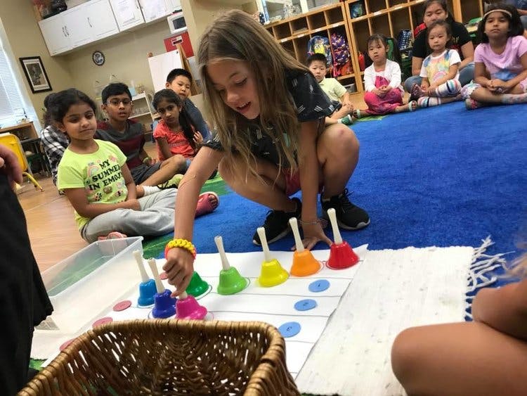 Child playing with colorful handbells while other children watch