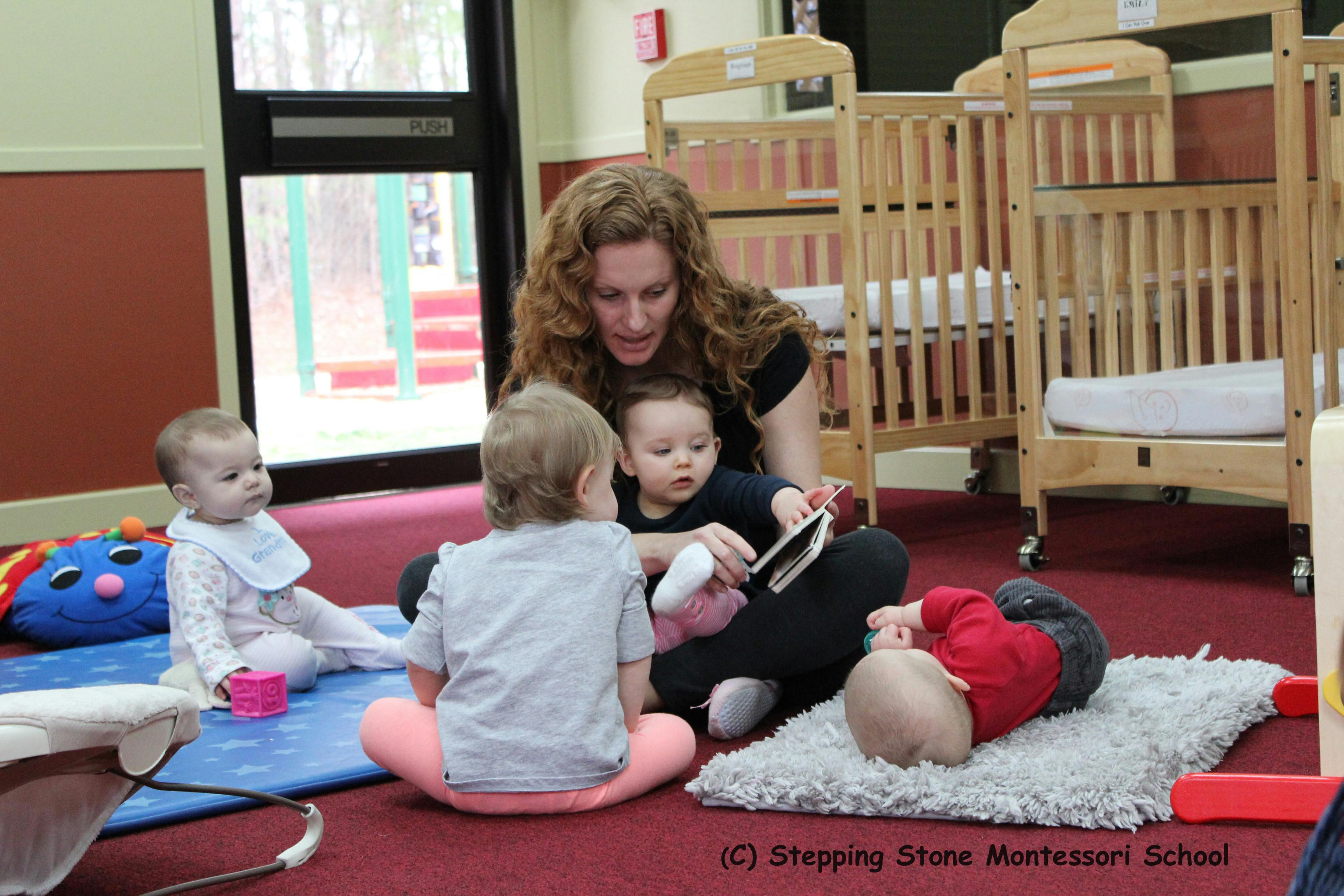 Person reading a book to three children in a classroom