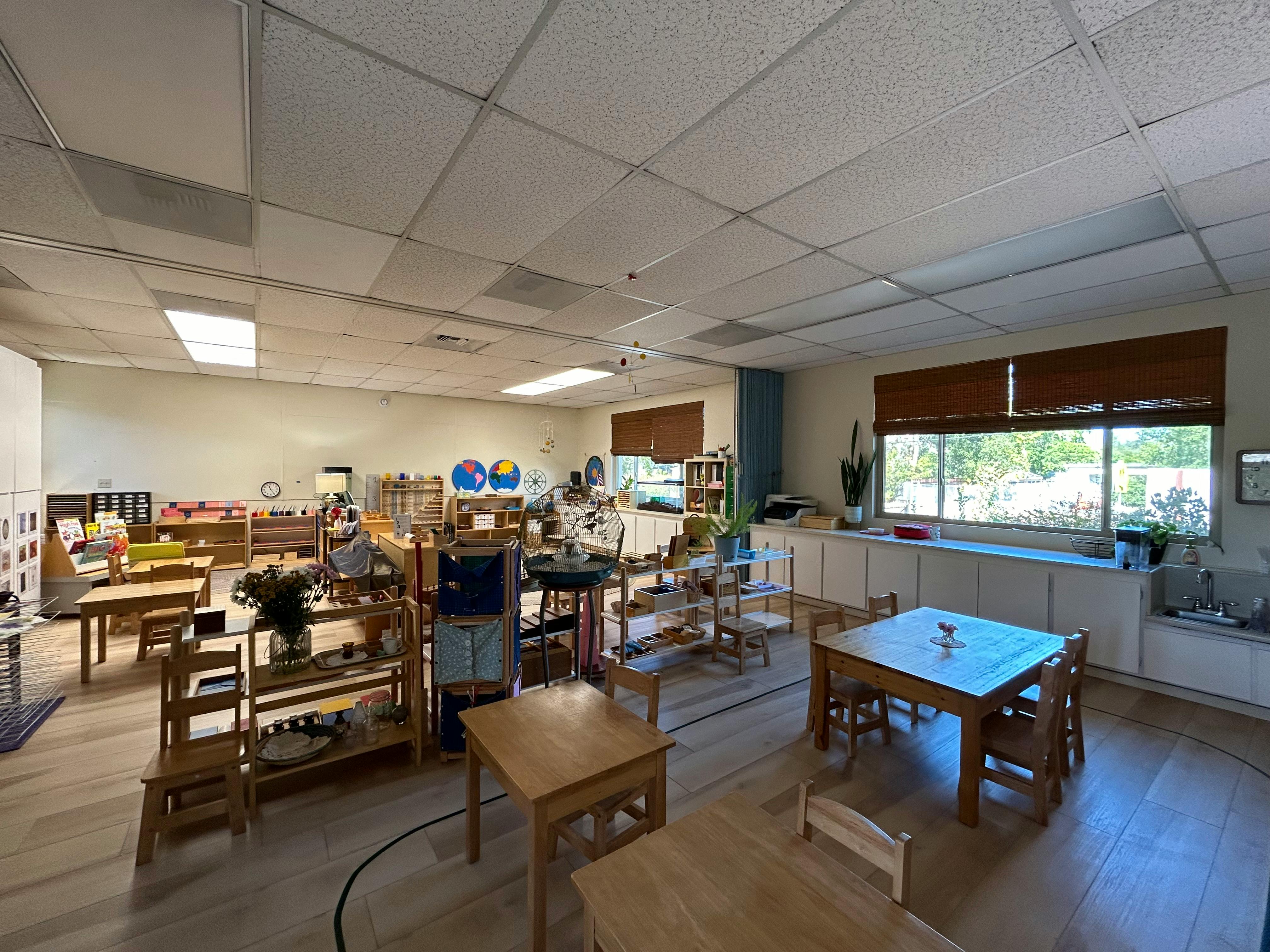 Classroom with small tables and chairs, shelves with learning materials